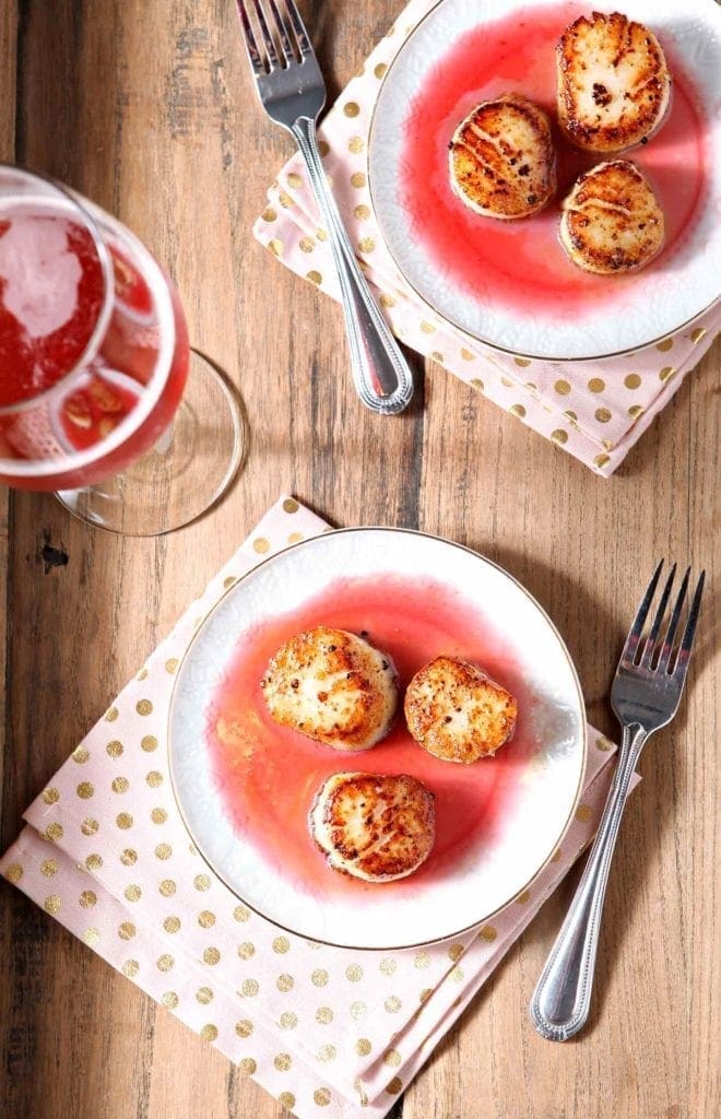 Overhead photo of Pan Seared Scallops with Raspberry Gastrique on a tray with pink drinks, napkins and forks