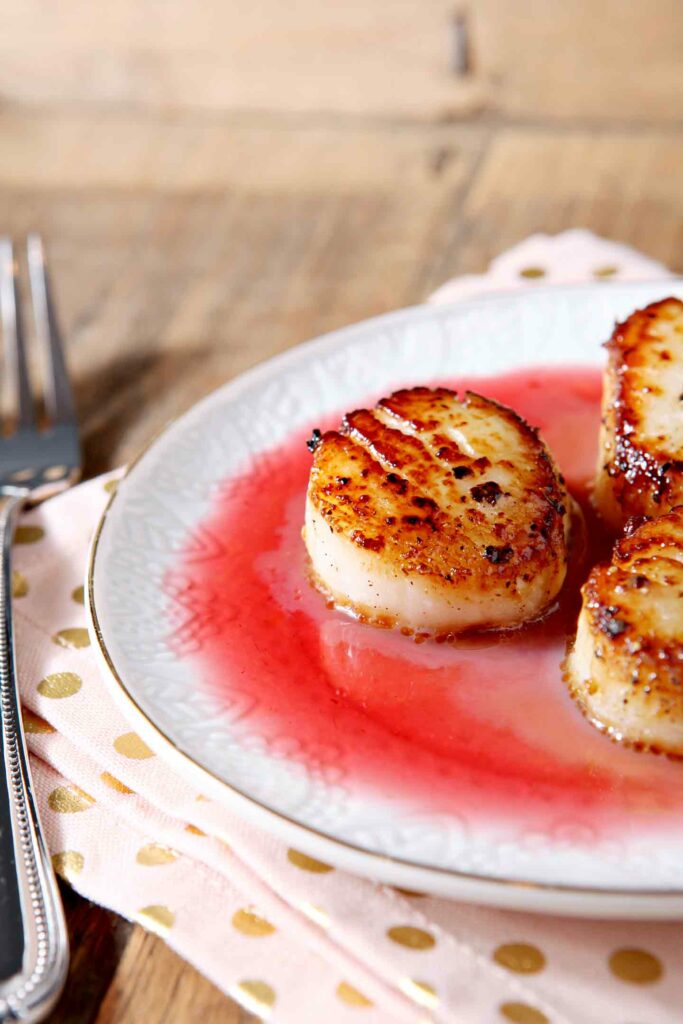 Close up of a pan seared scallop sitting on a white plate with raspberry gastrique