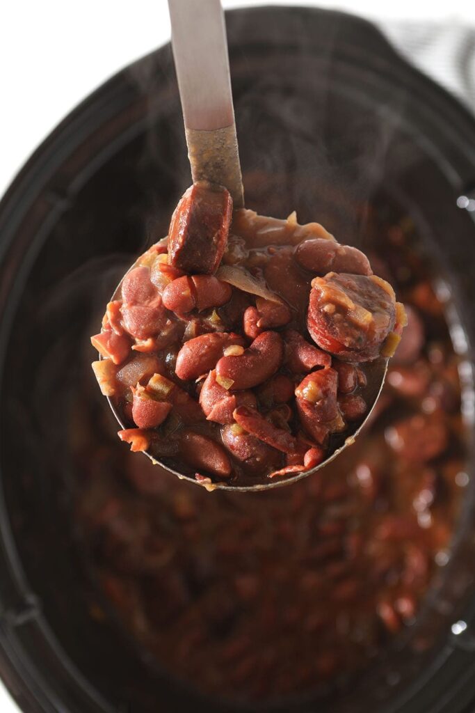 A ladle holds a scoop of red beans and rice above a slow cooker