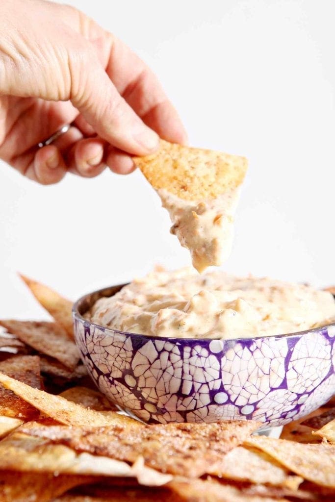 A woman dips a crispy cinnamon-sugar wonton into Carrot Cake Dip, served in a purple tiled bowl.