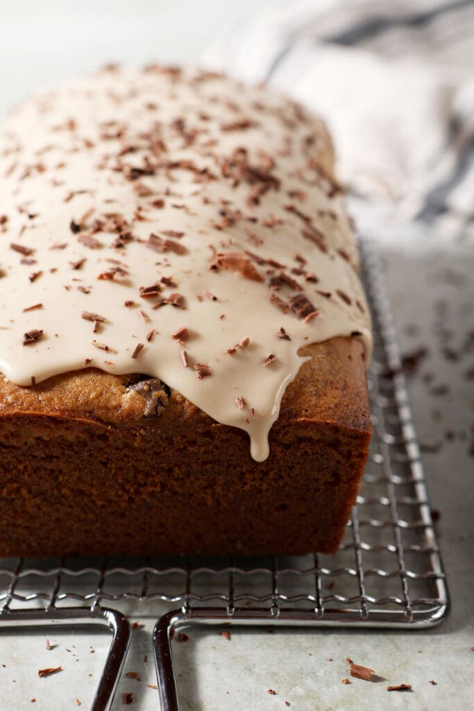 An Irish cream loaf cake with a drizzly icing topped with chocolate shavings on a light green countertop