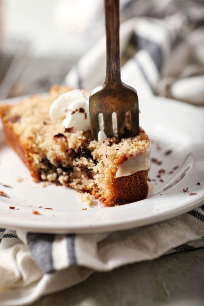 A fork cuts into a slice of chocolate chip loaf cake on a white plate