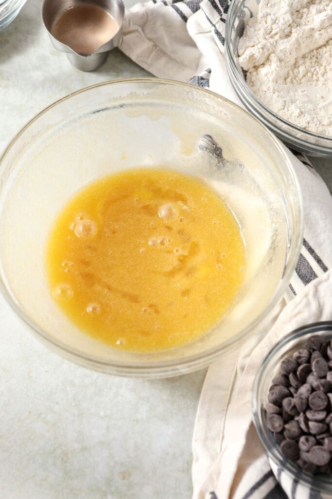 Wet ingredients in a bowl next to bowls of dry ingredients and chocolate chips