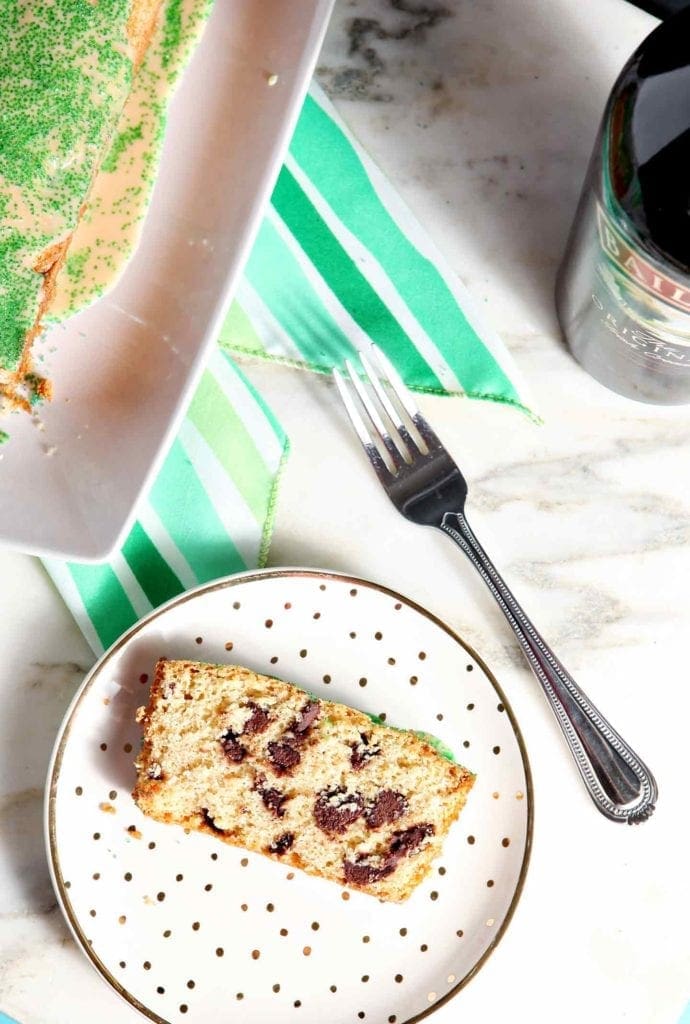 A slice of chocolate chip loaf cake sits on a gold and white plate next to a fork and a plate holding more cake