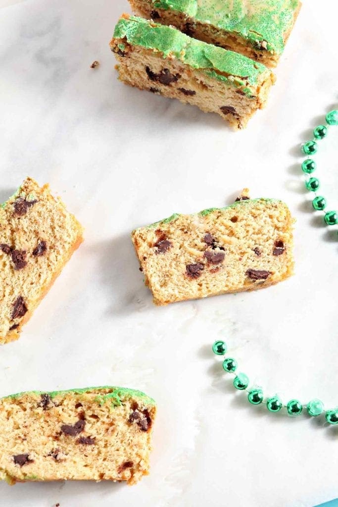 Several slices of a chocolate chip loaf cake sit on a marble surface next to a green set of beads