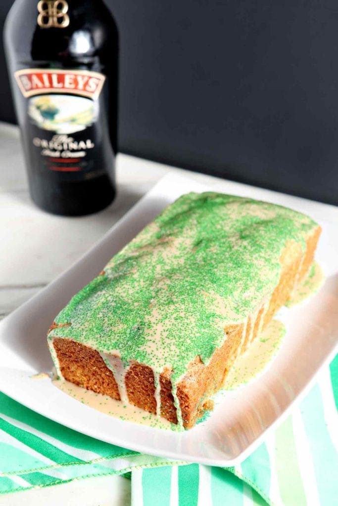 A loaf cake with an Irish Cream Glaze sits on a white plate next to a bottle of Irish Cream