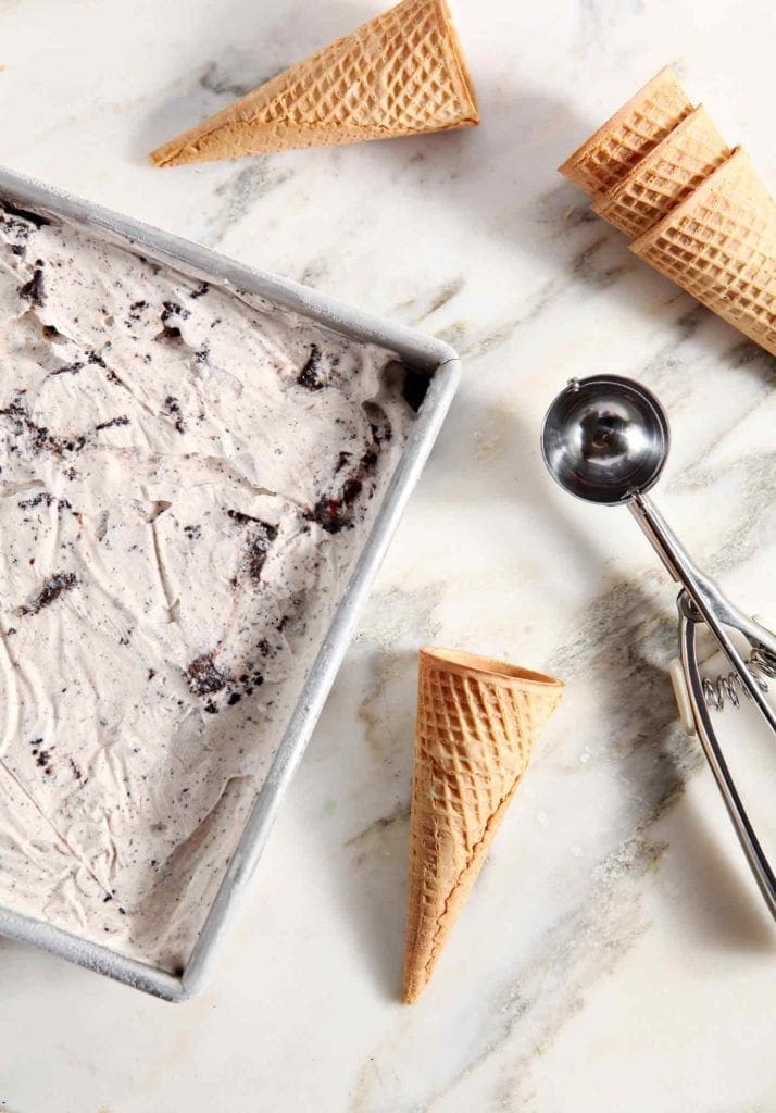 Frozen ice cream is shown with an ice cream scoop and cones