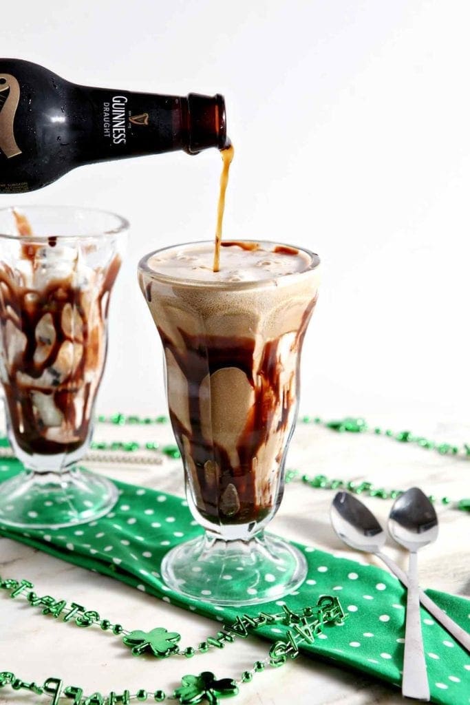 Beer pours into a glass holding ice cream and hot fudge sauce next to another glass