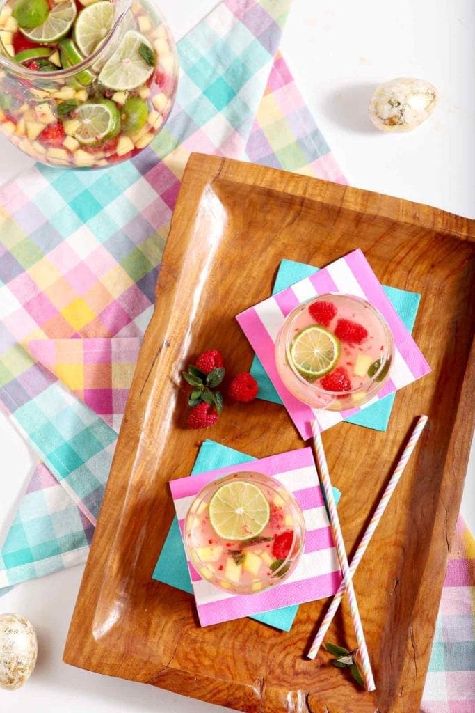 Two glasses of fruity sangria recipe on a wooden tray next to a pitcher