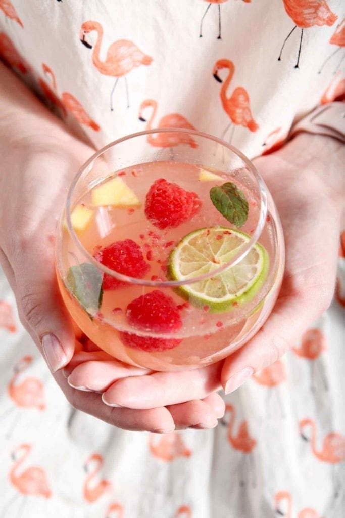 A woman in a flamingo shirt holds a glass of mango raspberry white wine sangria