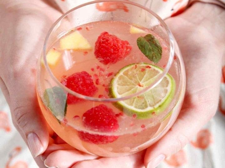 A woman in a flamingo shirt holds a glass of mango raspberry white wine sangria