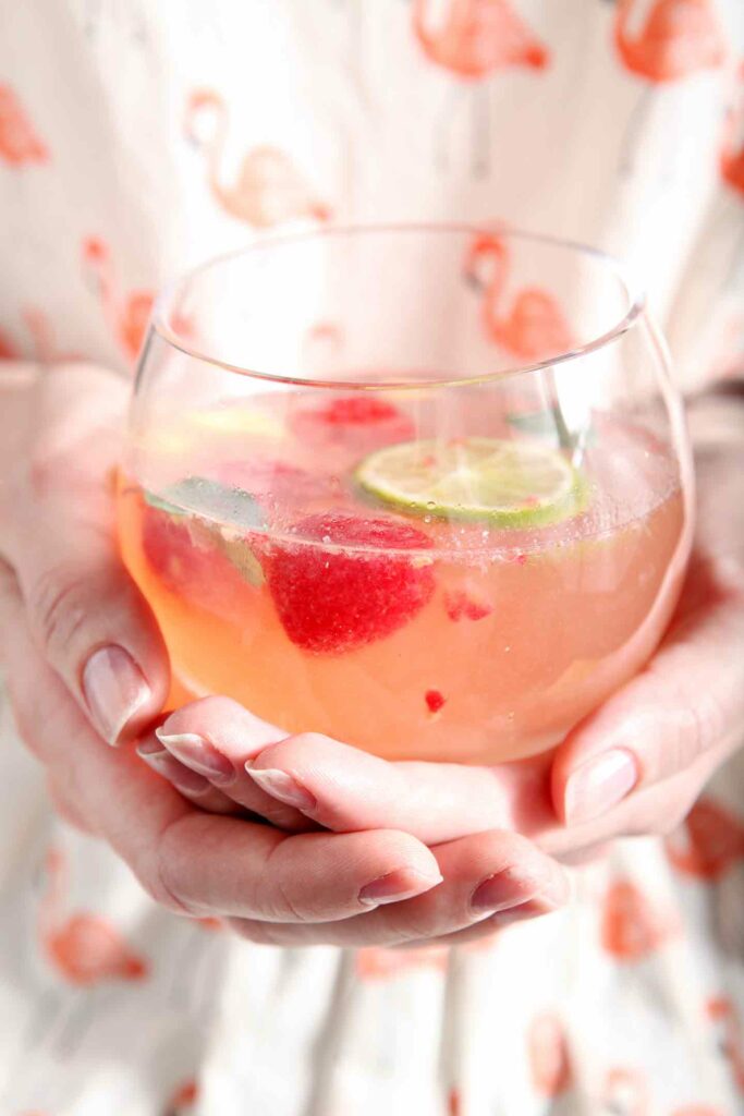 A glass of fruity sangria recipe is held in hand by a woman in a flamingo shirt