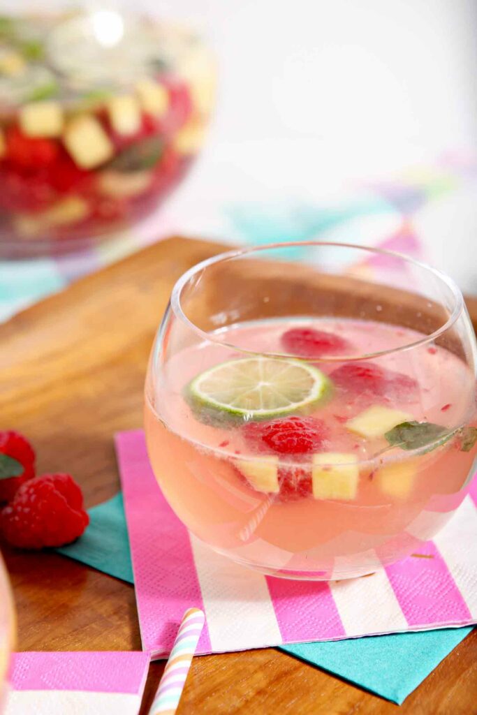 A glass of white wine sangria with raspberries and mango on a pink striped napkin