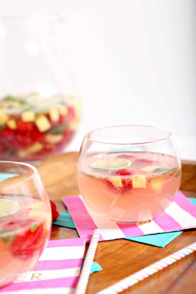 Two glasses of raspberry sangria on a wooden tray with colorful napkins and straws