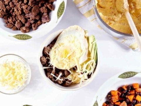 Southwestern Breakfast Burrito Bowl from above, with grits, ground turkey sausage, cheese, avocado, egg and a sweet potato hash on a white background