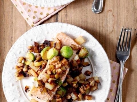 A plate of salmon topped with a vegetable hash on a wooden tray