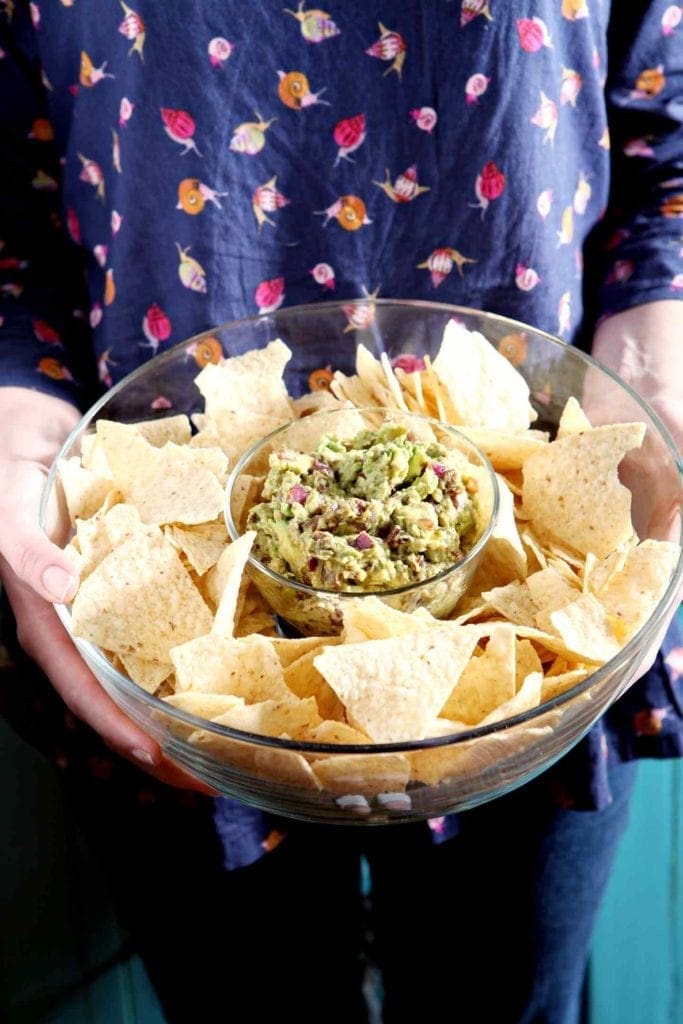 A woman holds a bowl of Caramelized Onion Guacamole with chips surrounding it