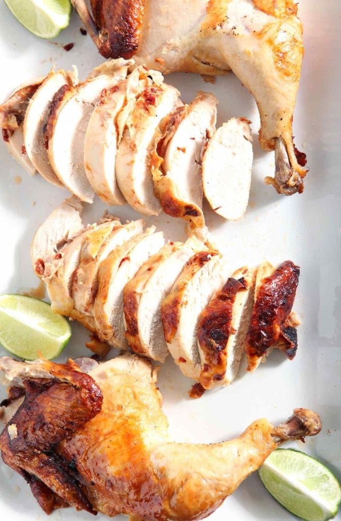 Sliced Chipotle Lime Spicy Beer Can Chicken is served on a white platter for dinner with lime wedges