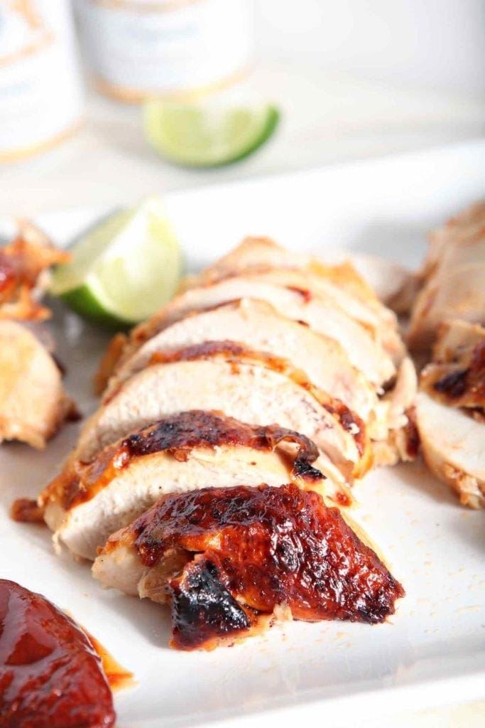 Sliced Chipotle Lime Spicy Beer Can Chicken sits on a white platter with lime wedges, ready to be plated and eaten