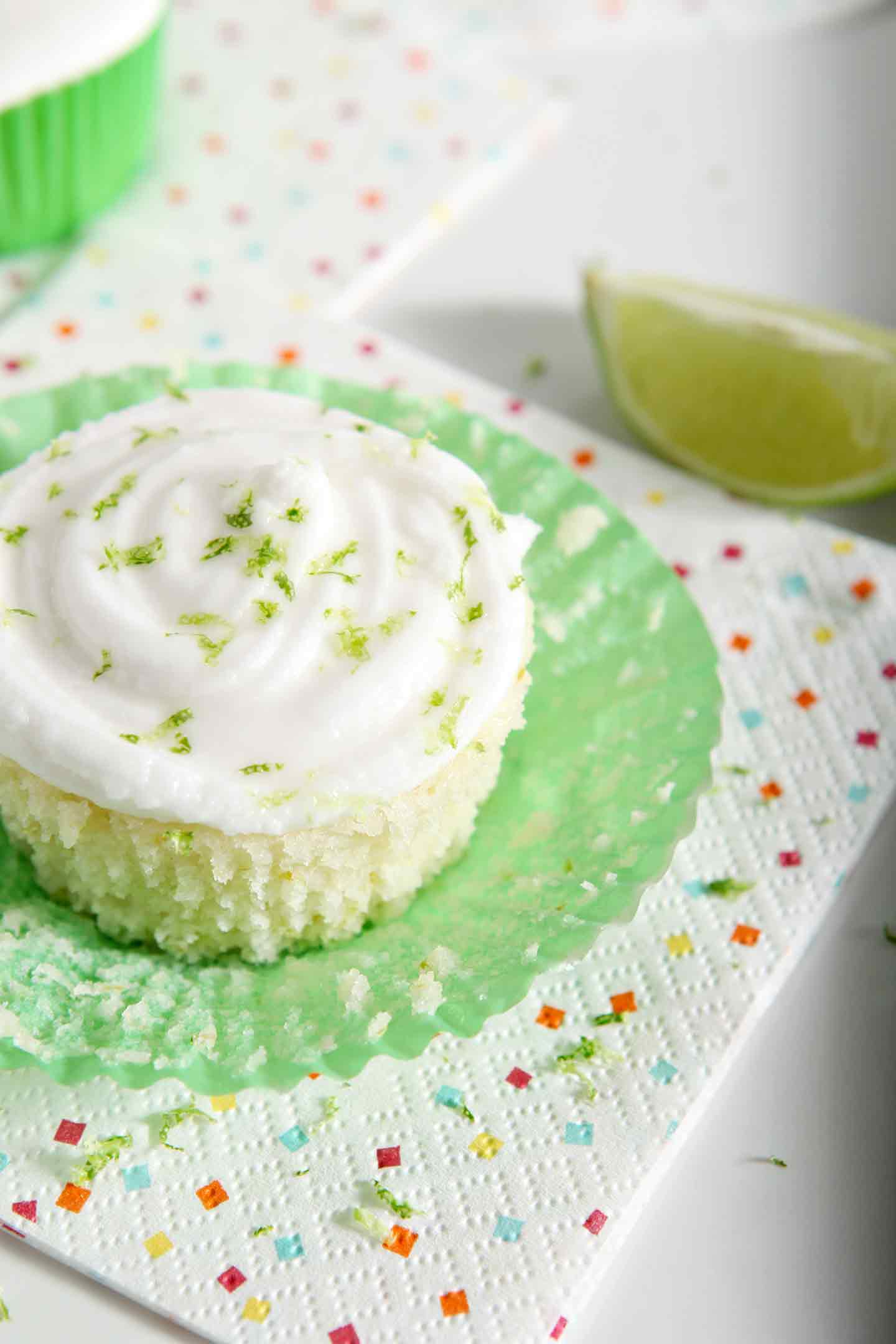 The cupcake liner of a lime cupcake is folded down. The final cupcake is sprinkled with margarita frosting and lime zest