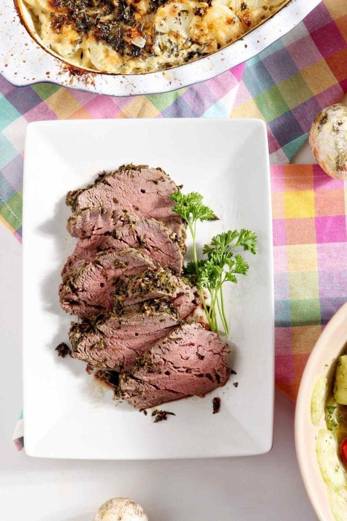 Sliced pieces of Mediterranean Herb Crusted Beef Tenderloin are served on a white platter