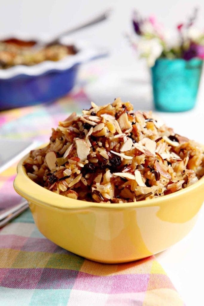 A yellow container holds Wild Rice Salad, surrounded by other dishes on a holiday table