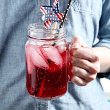 A woman holds a glass of Blackberry Tea, decorated with a patriotic pinwheel.