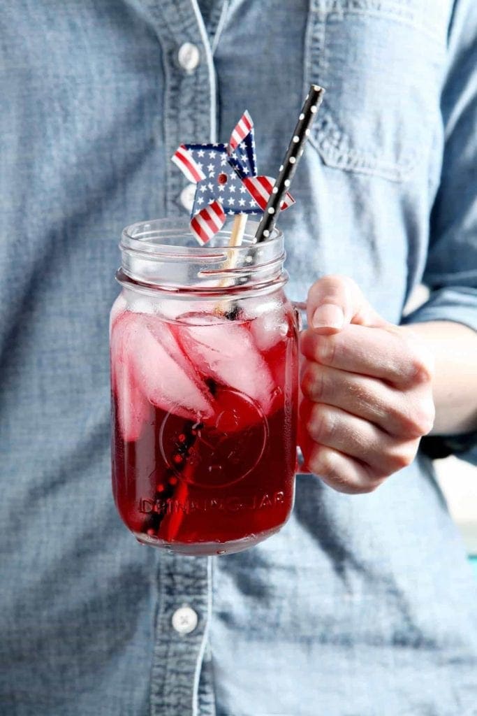 A woman holds a glass of Blackberry Tea, decorated with a patriotic pinwheel.