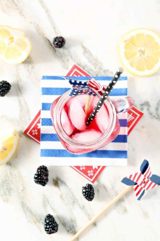 Overhead of a mason jar holding Blackberry Tea with a patriotic garnish on red, white and blue napkins on marble