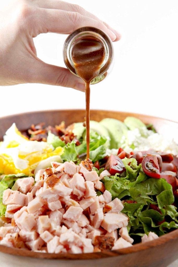 Homemade vinaigrette is drizzled onto a Cajun Cobb Salad before tossing.