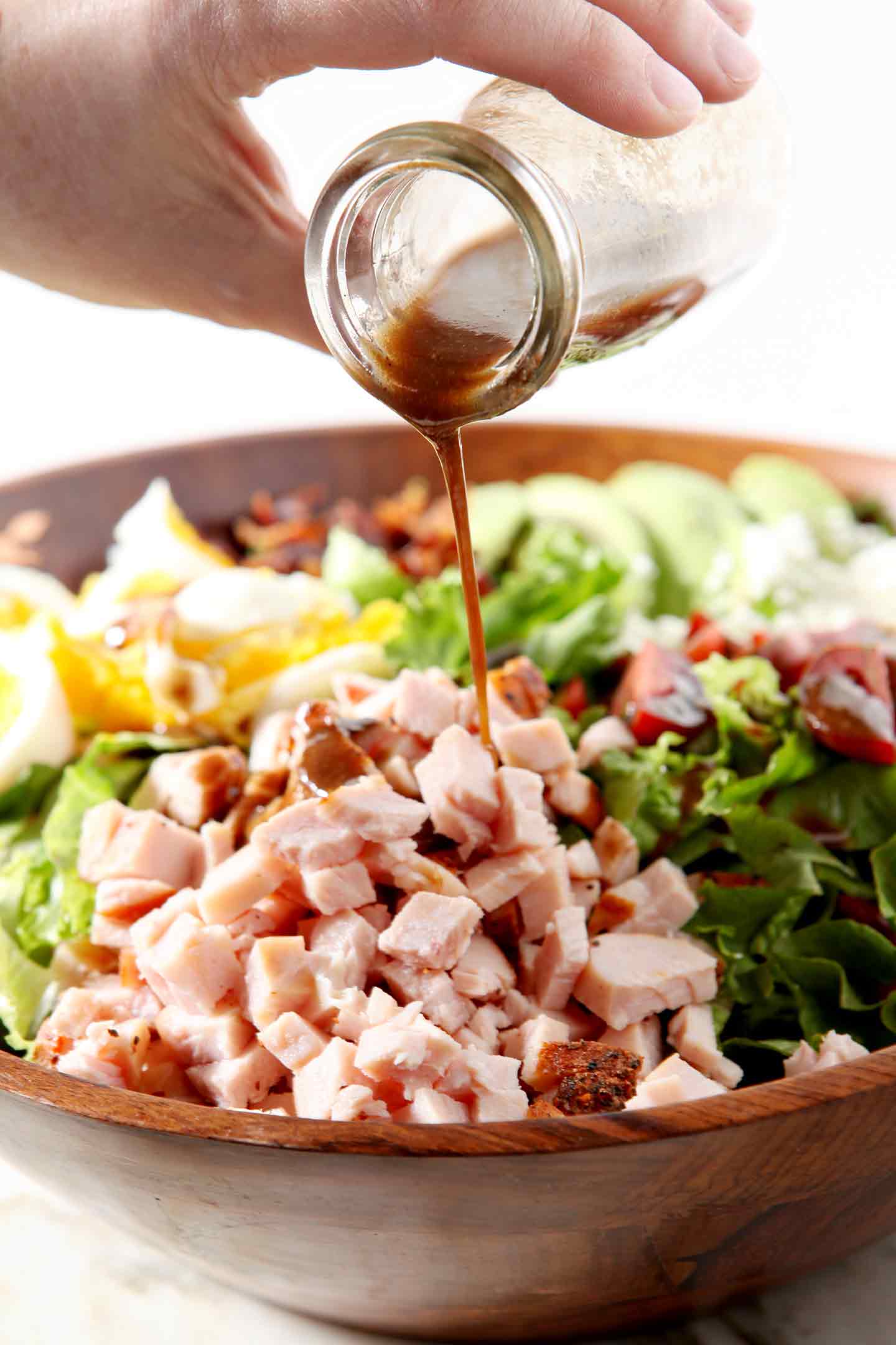 Homemade vinaigrette is drizzled onto a Cajun Cobb Salad before tossing.