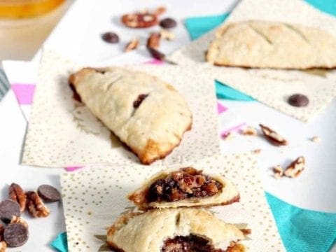 A Chocolate Bourbon Pecan Hand Pie is sliced in half and sits with two other hand pies on a white platter before serving
