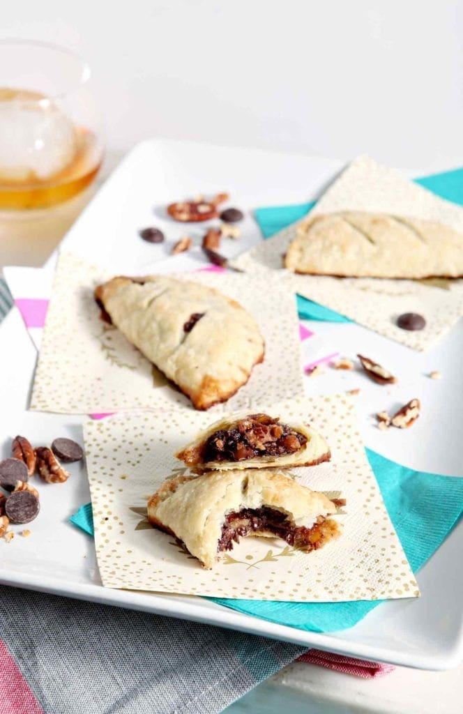 A Chocolate Bourbon Pecan Hand Pie is sliced in half and sits with two other hand pies on a white platter before serving