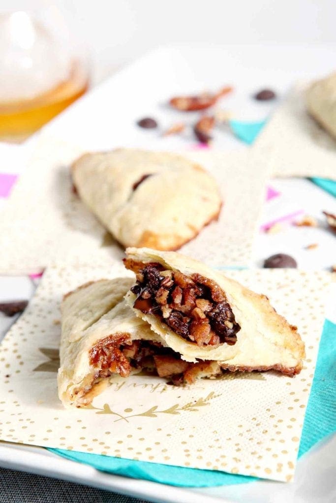 A Chocolate Bourbon Pecan Hand Pie is sliced in half and sits with two other hand pies on a white platter before serving