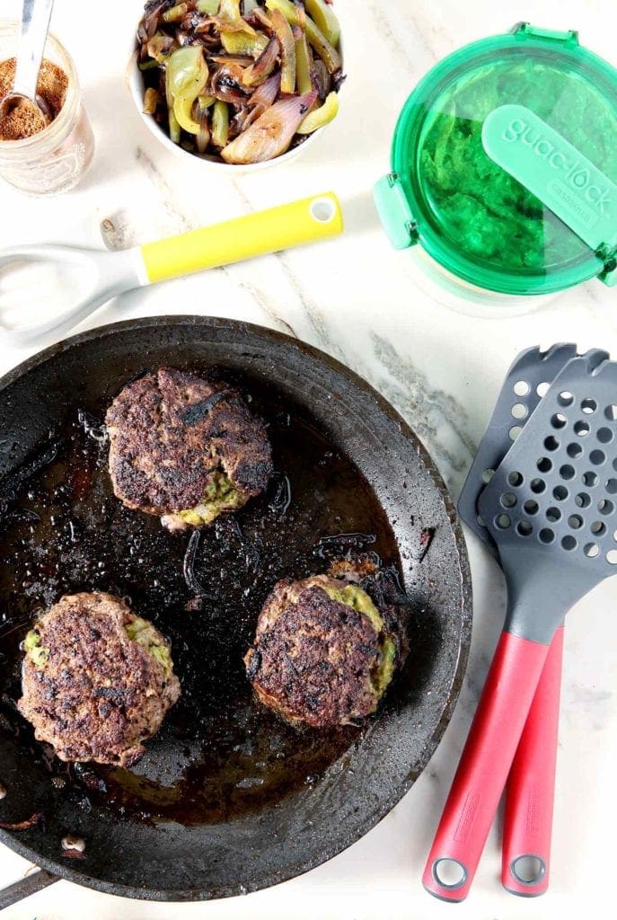 Burgers cook in a skillet, shown with burger toppings and tools