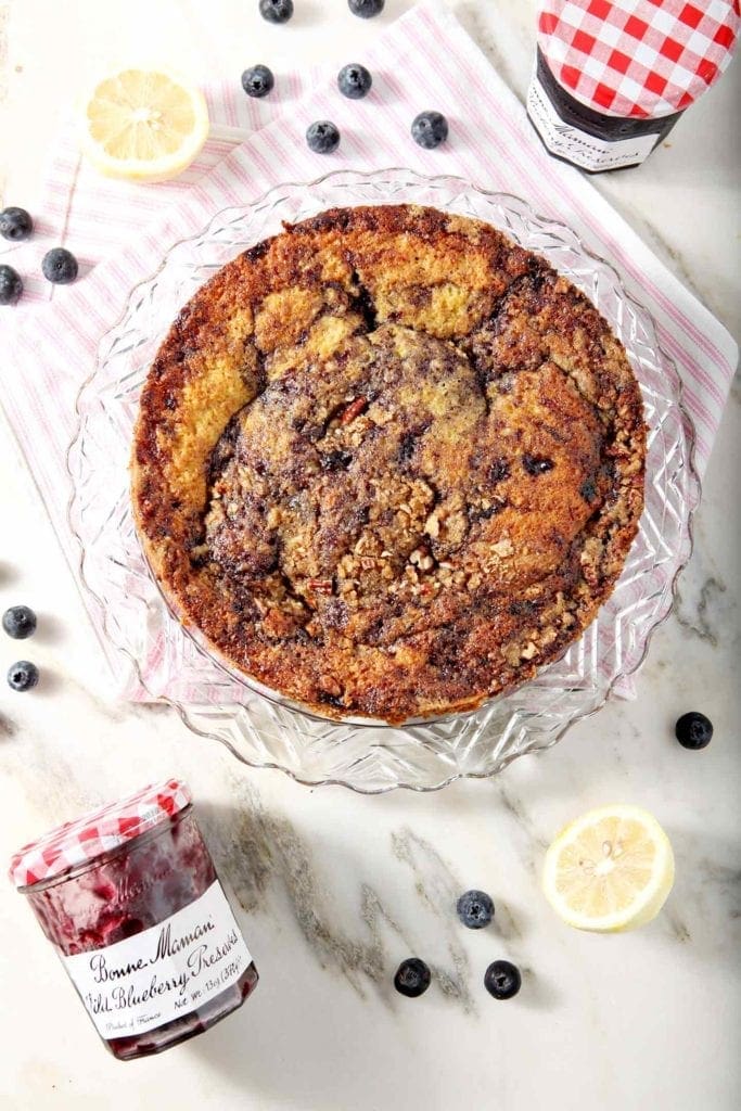 Overhead image of a whole Lemon Blueberry Coffee Cake before slicing, surrounded by lemons and blueberries