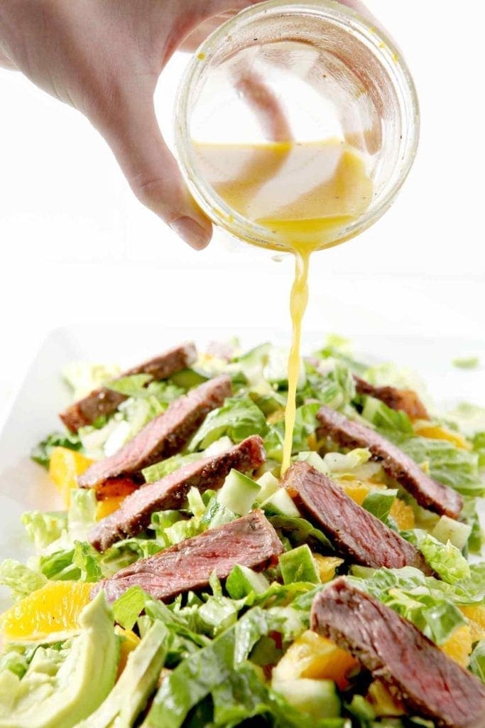 pouring salad dressing on a steak salad