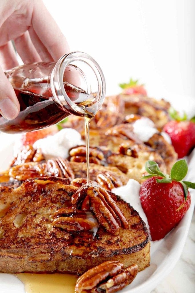 A woman pours maple syrup on the French toast