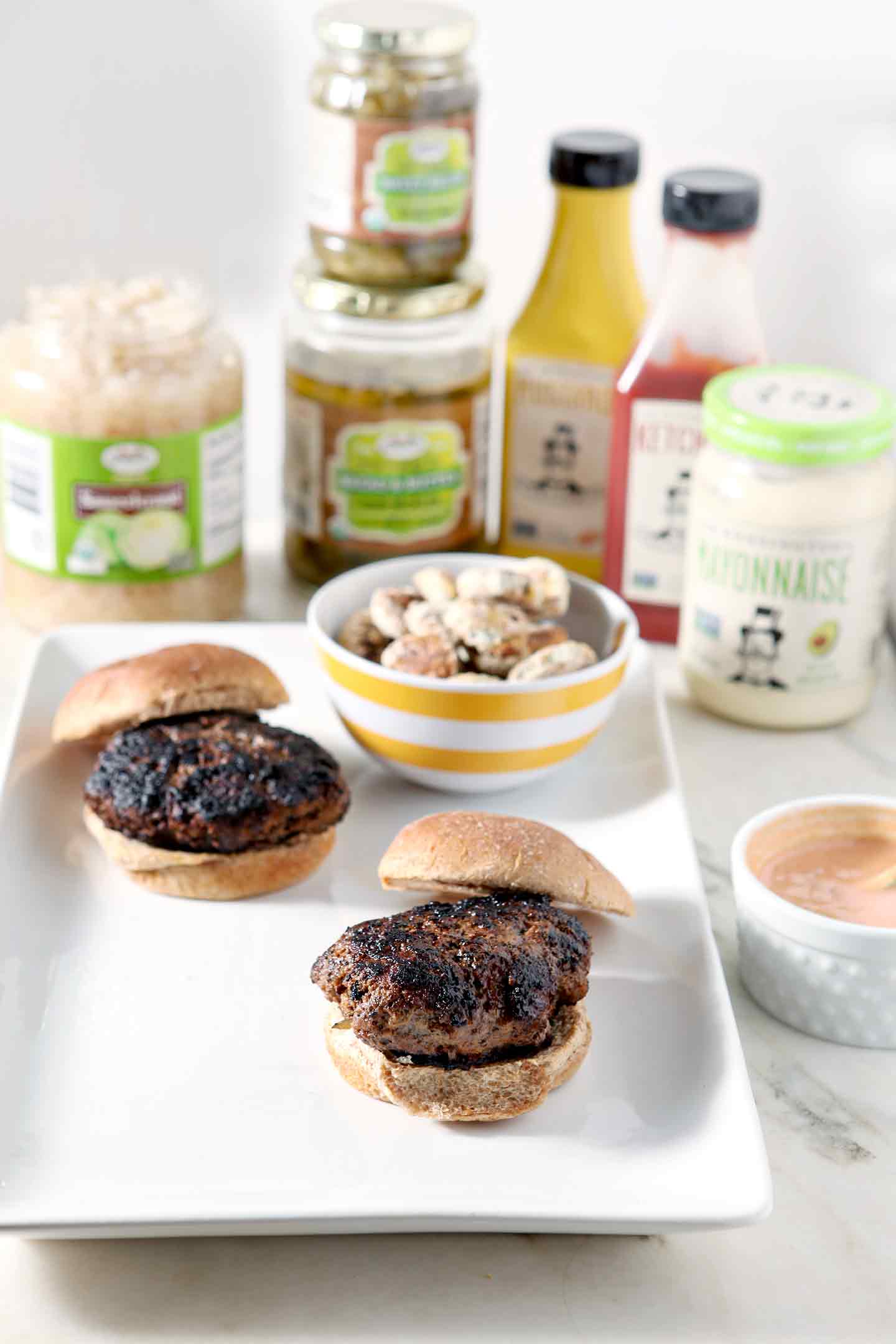 Two Sweet and Sauer Burgers are shown on a platter, surrounded by burger condiments and oven fried pickles