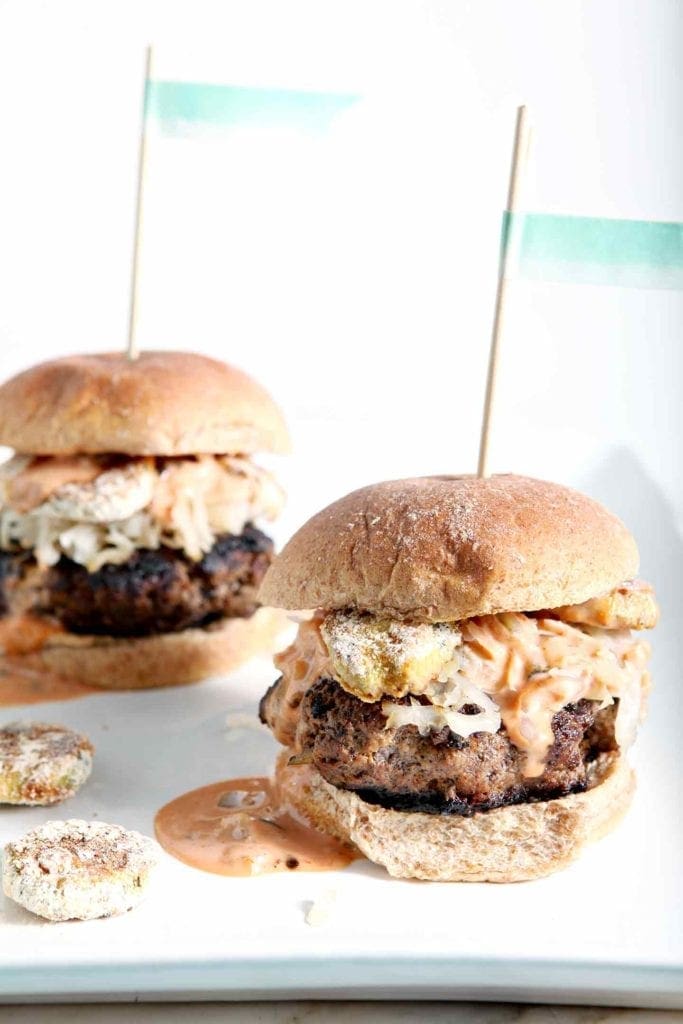 Two Sauerkraut Burgers with Oven Fried Pickles and Sweet Sriracha Sauce are shown on a platter, ready for eating