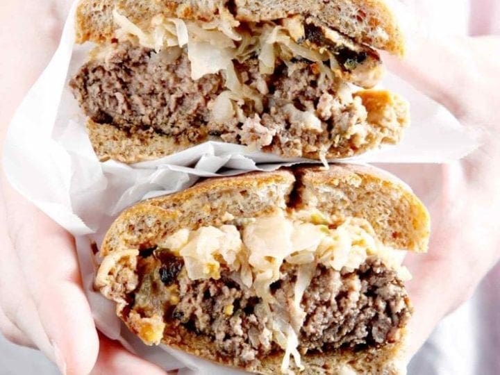 A halved Sauerkraut Burger with Oven Fried Pickles and Sweet Sriracha Sauce is held in hand before consuming