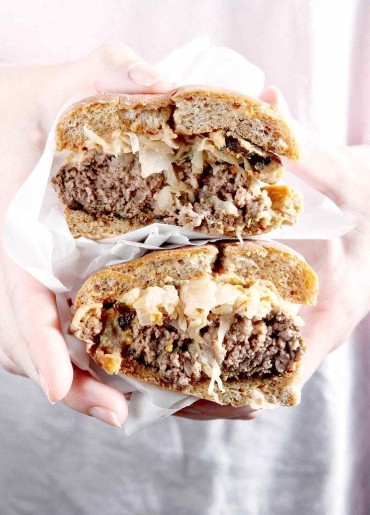 A woman holds a halved Sauerkraut Burger with Oven Fried Pickles and Sweet Sriracha Sauce 