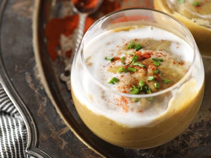 Close up of a clear glass bowl holding a serving of vegan potato leek soup garnished with additional coconut cream, paprika and chives