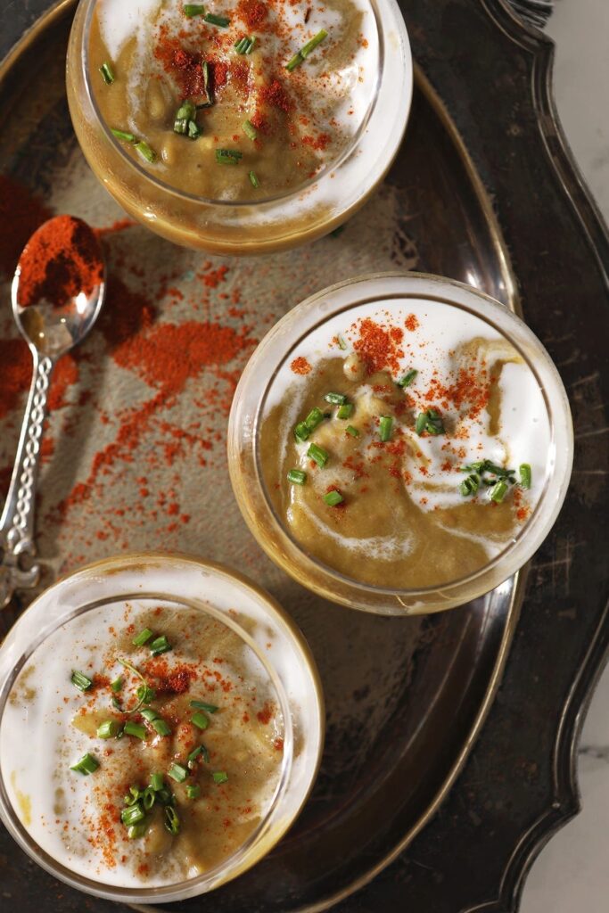 Three bowls of vegan potato leek soup from above on a silver tray next to a spoonful of paprika