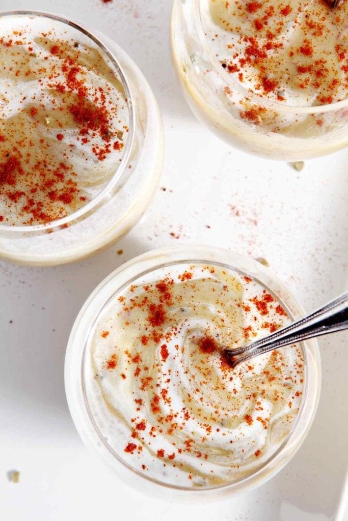 Overhead of three bowls of vegan potato leek soup garnished with extra coconut cream and paprika on a white tray