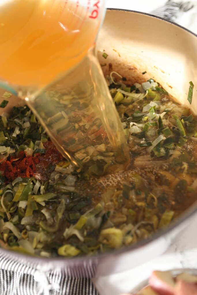 Vegetable stock pours on top of vegetables in a Dutch oven