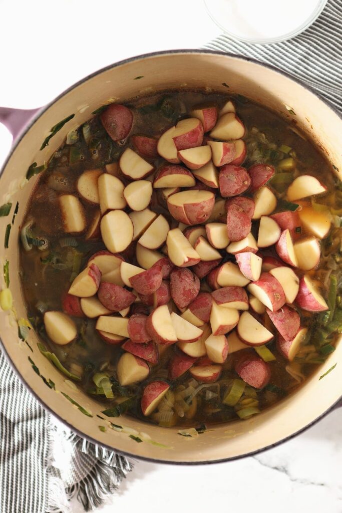 Chopped red potatoes sit on top of veggies and liquid in a Dutch oven