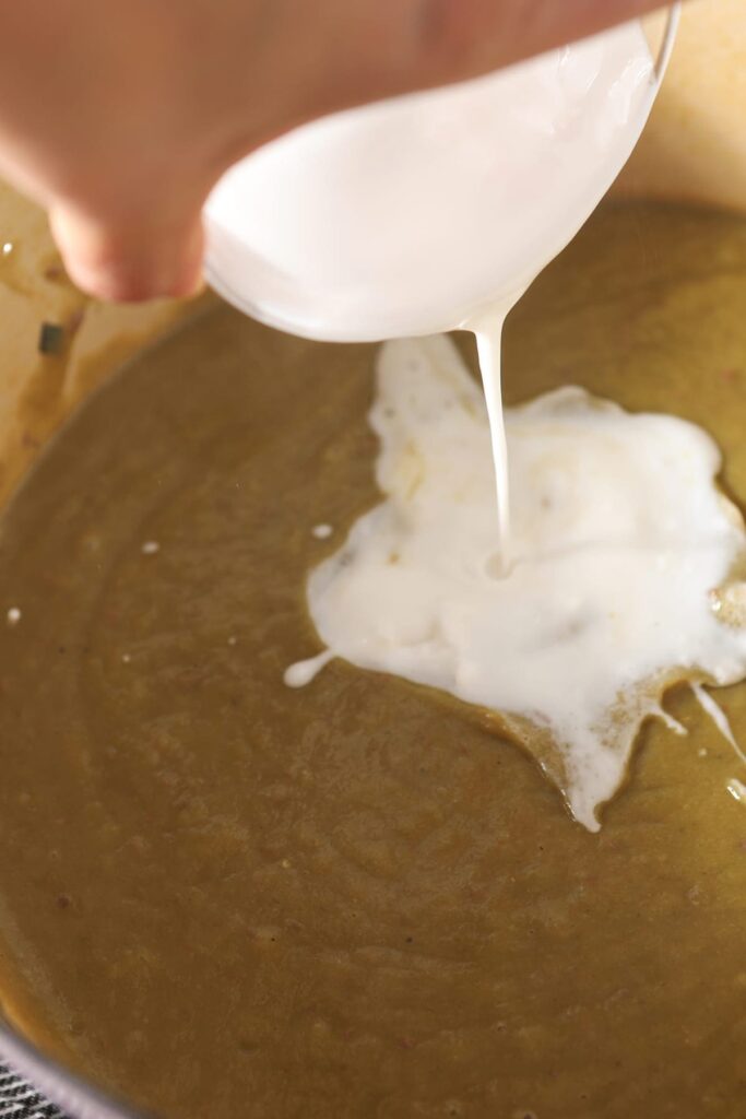 Coconut cream pours on top of soup in a Dutch oven