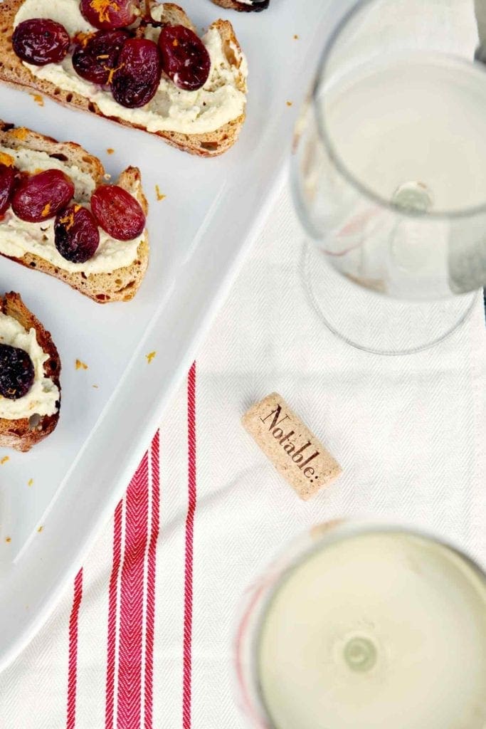 wine in a glass and roasted grape bruschetta on a white plate