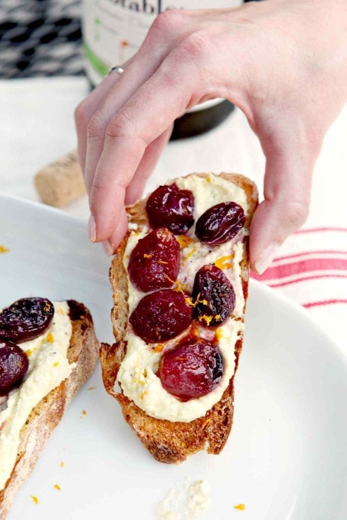 hand picking up roasted grape bruschetta